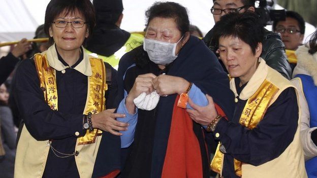 A grieving relative of a victim in the recent commercial plane crash is led by volunteers at a funeral hall in Taipei, Taiwan, Thursday, Feb. 5, 2015