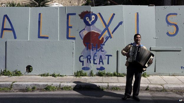 A busker plays in front of a sign supporting Greek PM Alexis Tsipras (21 Feb)
