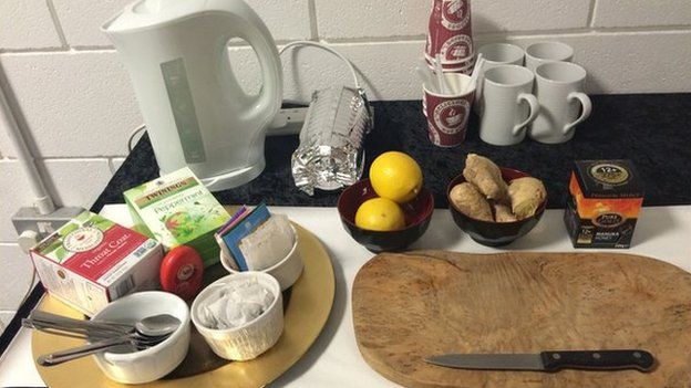 A kettle, cups, lemons, ginger root, and a selection of tea bags on a table