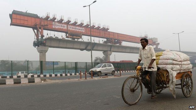 Indian tricycle rickshaw puller passes by an under construction elevated Delhi Metro section in New Delhi.