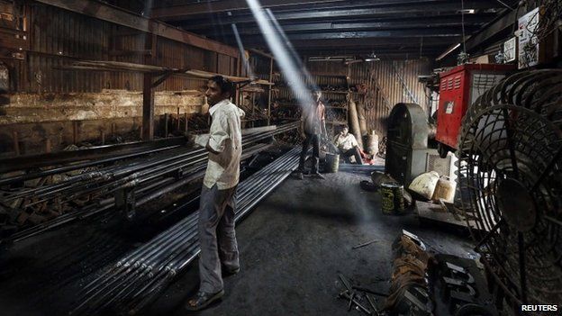 A worker carries an iron pipe inside a metal fabrication workshop in an industrial area of Mumbai February 9, 2015.