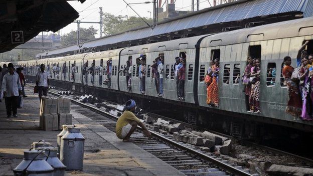 Indian passengers hang from the doors of the coaches of a crowded local train on the outskirts of Kolkata, India, Thursday, Feb. 26, 2015