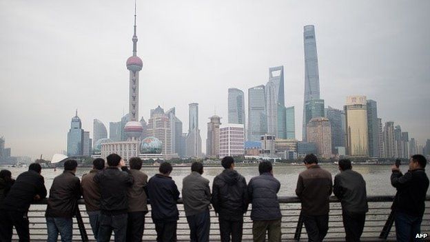 Chinese tourists stand along the promenade on the Bund overlooking the Huangpu River against the skyline of the Pudong district in Shanghai on December 10, 2014.