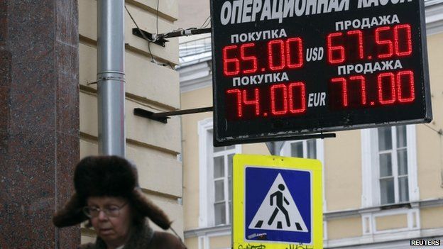 A woman walks near a board displaying currency exchange rates in Moscow