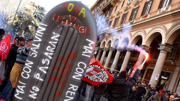 A protester holds a burning flare next to an inflatable boat with slogans written on it during the Never with Salvini counter-demonstration organised by left-wing groups in Rome, 28 Feb