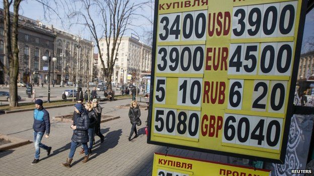 People walk past a board showing currency exchange rates in central Kiev 25 February 2015