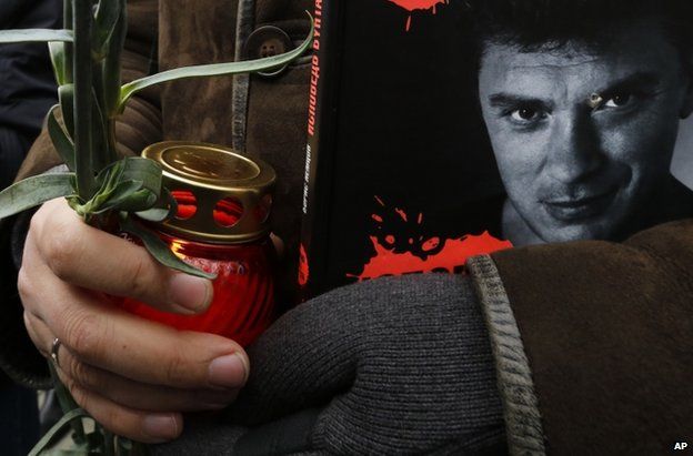 A woman clutches a votive candle and a book bearing Boris Nemtsov's portrait at his funeral in Moscow, 3 March