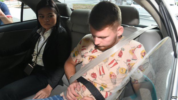 A policewoman sits next to Elton Hinz, one of the two German nationals arrested in Singapore for vandalism, as they arrive in a police car to the state court on 22 November 2014