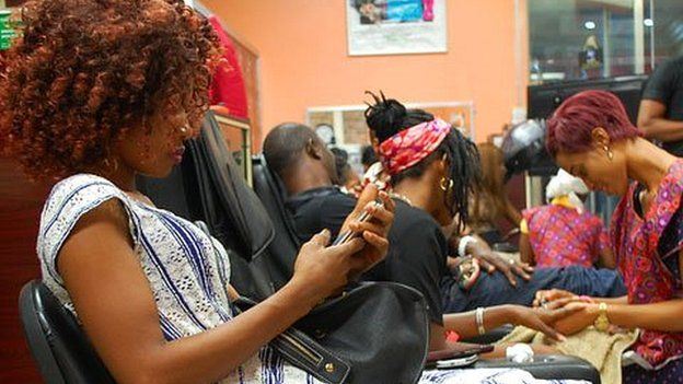 A customer reading her phone at Bruno's Place hair salon in Ikeja Mall in Lagos, Nigeria
