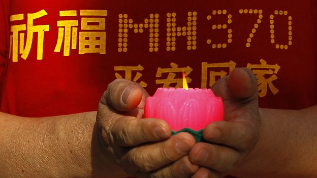 Person holding a candle and wearing a T-shirt with MH370 written on it