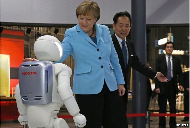 German Chancellor Angela Merkel (C), escorted by Mamoru Mori, executive director of the museum and former astronaut, touches "Asimo", a bi-ped humanoid robot developed by Honda Motor Co., while visiting Miraikan (National Museum of Emerging Science and Innovation) in Tokyo 9 March 2015.
