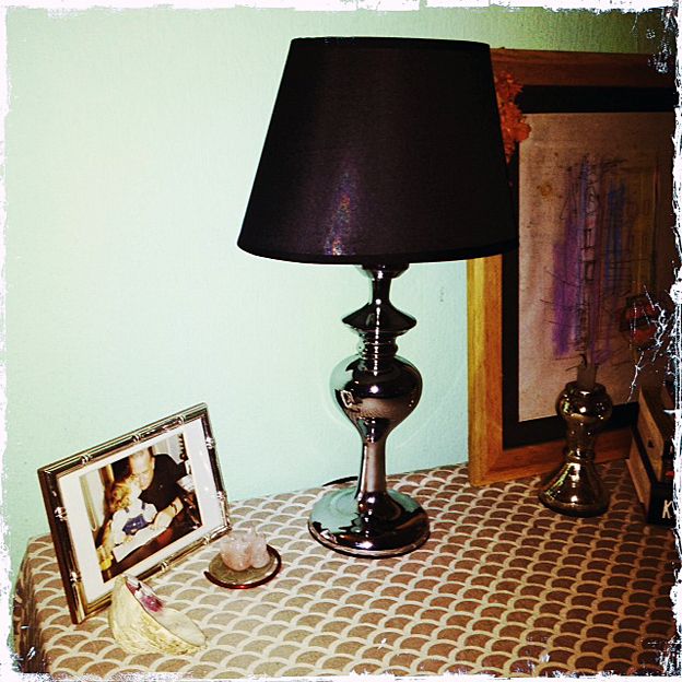 A table with a picture frame, lamp and red bangle