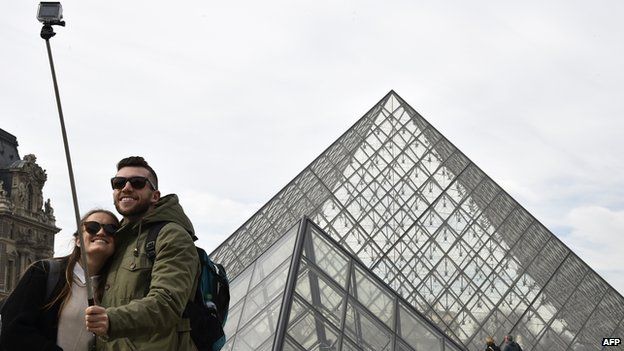 Tourists use selfie stick outside The Louvre