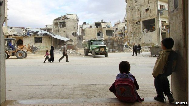 Schoolchildren watch workers clear rubble of damaged buildings off a street in the Douma neighbourhood of Damascus - 4 March, 2015