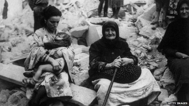 Greeks sit among the ruins of homes in 1940