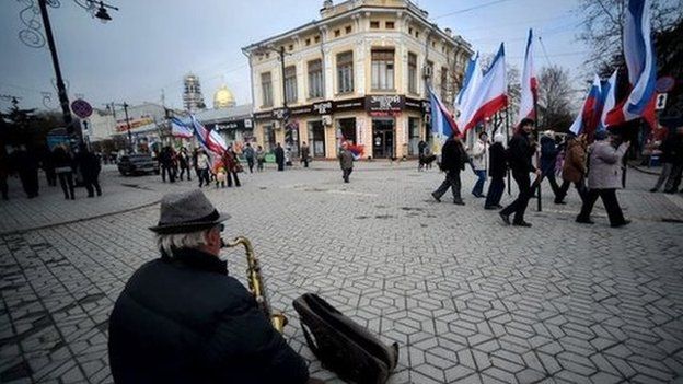 A man playing a saxophone as people waving Russian and Crimean flags walk to a pro-Russia rally in Simferopol's Lenin Square on 9 March 2014