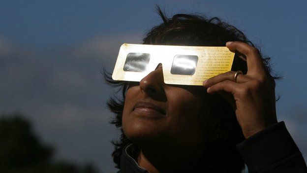 A woman looks at a partial eclipse of the sun through special glasses, from Hyde Park in London