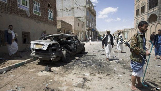 Houthi rebels stand near a damaged car after a bomb attack in Sanaa, Yemen, 20 March 2015