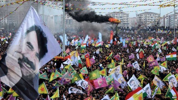 Smoke rises from a fire burning as people wave Kurdish flags and pictures of jailed Kurdish rebel leader Abdullah Ocalan as they gather to celebrate Newroz, the Kurdish New Year, in the south eastern Turkish city of Diyarbakir, 21 March 2015