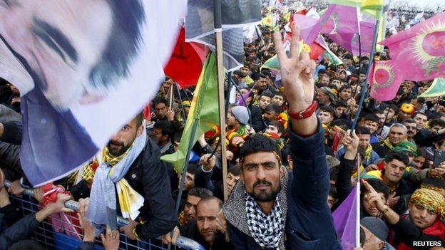 People gesture while others wave Kurdish flags and pictures of Abdullah Ocalan, during a gathering celebrating Newroz in Diyarbakir, Turkey, 21 March 2015