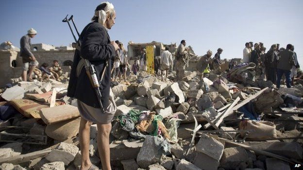 A Houthi fighter stand guard as people search for survivors under the rubble of houses destroyed by Saudi airstrikes near Sanaa airport, Yemen, Thursday, 26 March 2015