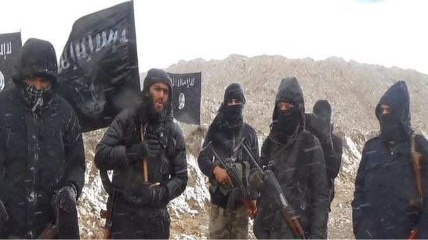 A group of men, mostly masked, standing under an Islamic State flag. Ifthekar Jaman is the only person whose face can be seen
