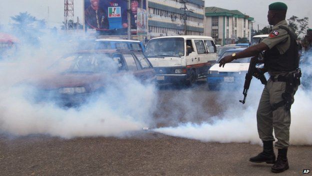 A Nigerian soldier stands next to a tear gas canister as it sprays gas into traffic during a protest by members of the All Progressives Congress
