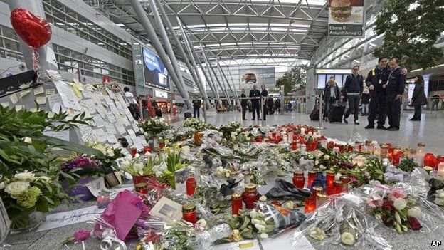 Passengers pass by candles and flowers for the victims of the plane crash at the airport in Dusseldorf (31 March 2015)