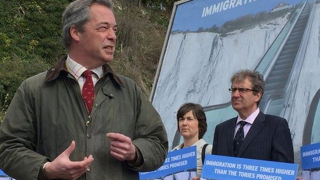 Nigel Farage stands in front of immigration poster