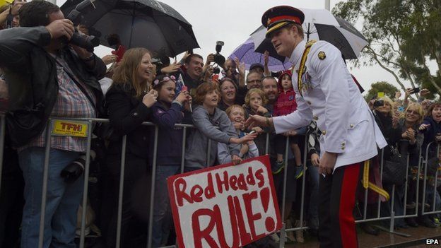 Prince Harry meeting a crowd in Australia. A sign says "red heads rule".