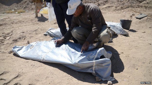 A member from the Iraqi forensic team writes on a body bag containing remains belonging to Shia soldiers from Camp Speicher killed by Islamic State militants at a mass grave in the presidential compound of the former Iraqi president Saddam Hussein in Tikrit on 6 April 2015