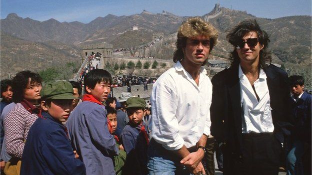 Young children sporting 'Mao' jackets and caps gape at George Michael (left) and Andrew Ridgeley, of the pop group Wham who are visiting the Great Wall as they promote the first-ever gig by a Western pop band in communist China, on 7 April 1985.