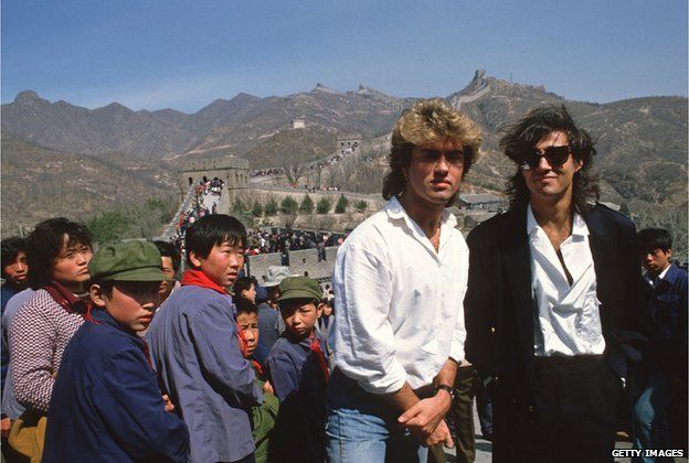 Young children sporting 'Mao' jackets and caps gape at George Michael (left) and Andrew Ridgeley, of the pop group Wham who are visiting the Great Wall as they promote the first-ever gig by a Western pop band in communist China, on 7 April 1985. (DO NOT REUSE IMAGE)