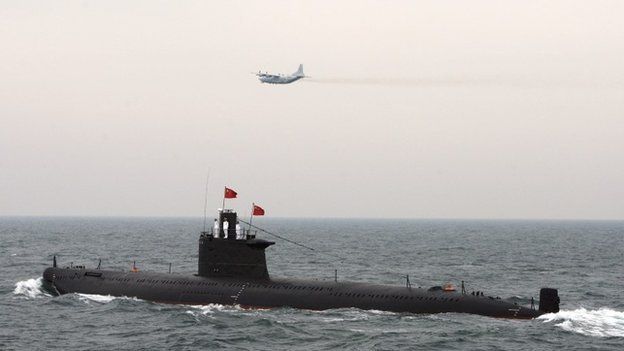 A military aircraft flies past a Chinese Navy submarine