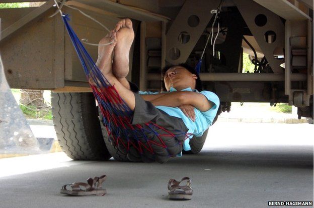 A man sleeps with his hammock underneath a truck