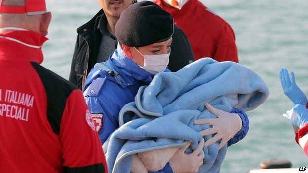A Red Cross volunteer carries a baby wrapped in a blanket after migrants disembarked at the Sicilian Porto Empedocle harbor, Italy, 13 April 2015