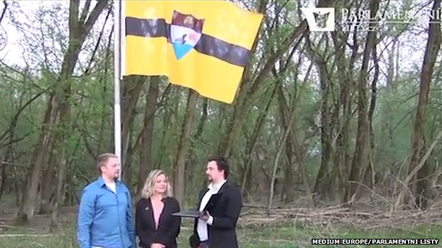 The "founders" of Liberland standing in front of the raised flag