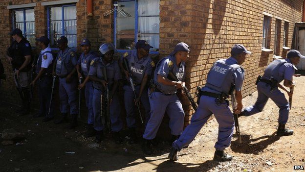 Police officers advance to enter men's hostel after xenophobic violence in the area overnight forced foreign shop owners to close their shops for fear of attack in Actonville, Johannesburg on 16 April 2015