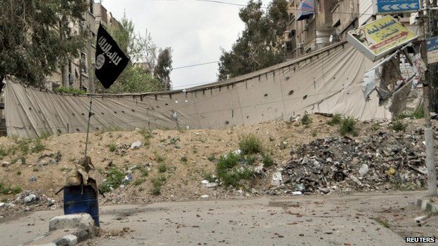 An Islamic State flag is seen near a barricade, which serves as protection from snipers of forces loyal to Syria"s President Bashar al-Assad, in Yarmouk Street, the main street of Yarmouk camp, April 10, 2015
