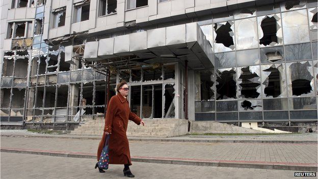 A woman walks past a building damaged by fighting in Donetsk on 15 April, 2015