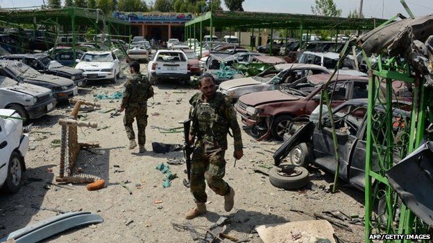 Afghan security personnel walk through the site of a suicide car bomb attack targeting a NATO convoy near the airport in Jalalabad on April 10,2015