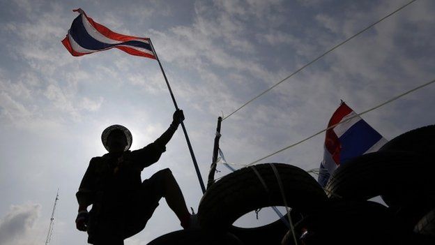 An anti-government protester holds a flag on a barricade as policemen gather in front of it near the Government House in Bangkok 18 February, 2014