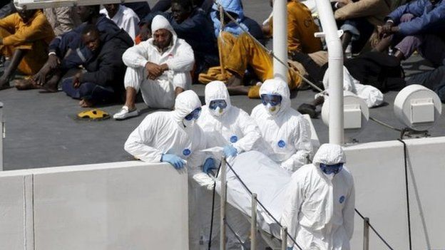 Armed Forces of Malta personnel in protective clothing carry the body of a dead immigrant off Italian coastguard ship Bruno Gregoretti as surviving migrants watch
