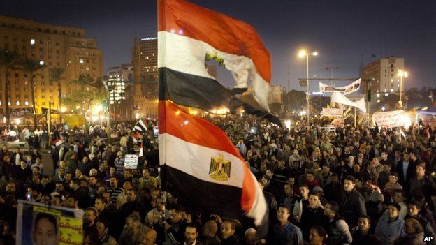 Egyptians opposing president Mohammed Morsi fly their national flags as one holds a poster with a picture of a slain protester with Arabic that reads "Martyr Mostafa Helmi, down with the rule of the Morshid," during a rally in Tahrir Square, Cairo, Egypt, Tuesday, Dec. 18, 2012