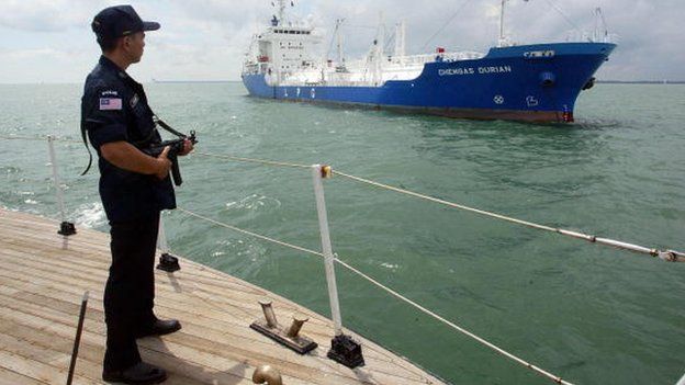 An armed Malaysian marine policeman standing guard on the deck of his patrol boat while patrolling past a tanker in the Malacca Strait, July 3, 2003