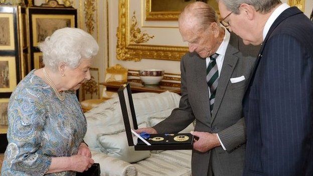 Queen Elizabeth II presents Prince Philip with the Insignia of a Knight of the Order of Australia with Australian High Commissioner Alexander Downer
