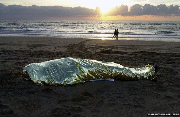 Fuerteventura, 2003 - a body lies on the beach as tourists go for a walk
