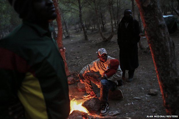 A migrant warms himself by a fire at a clandestine campsite in northern Morocco near the border fence with Spain's North African enclave Melilla, 2013