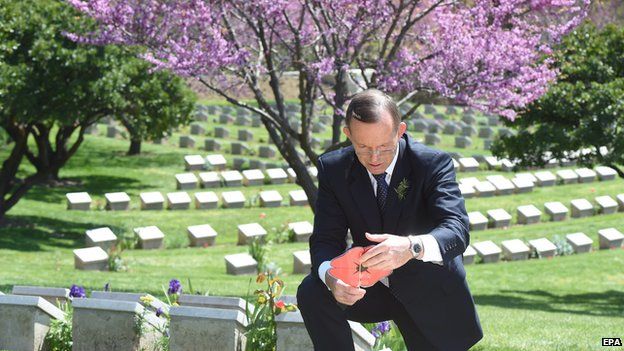 Australian Prime Minister Tony Abbott reads a paper poppy