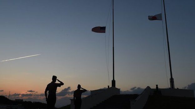 Servicemen of US Marine Corps salute while Japanese (R) and US flags are being taken down at the evening colors ceremony at the Camp Foster near Futenma Base in Ginowan, Okinawa prefecture, on November 14, 2014.